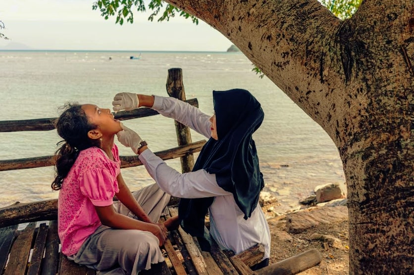 Rani Amsa, bidan dari Puskesmas Peukan Bada, memberikan imunisasi polio di dekat pantai di Aceh Besar, Aceh, saat Pekan Imunisasi Nasional pada bulan Desember 2022. Foto: WHO/Fauzan Ijazah